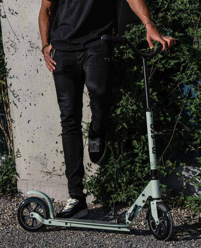 man leaning against a wall with his clay speed plus deluxe adult scooter