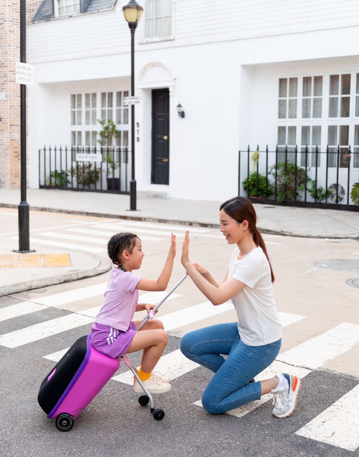 mum and daughter high fiving while riding the violet luggage suitcase